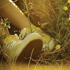 a pair of yellow tennis shoes sitting in the grass with daisies growing around them