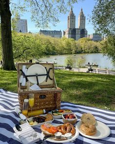 a picnic table with food and drinks on it in the park next to a body of water