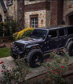 a black jeep parked in front of a brick building with roses growing on the sidewalk