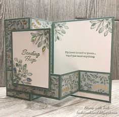 an open card with flowers and leaves on the inside is shown in front of a wooden background