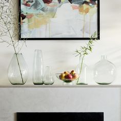 a fireplace with vases and fruit on it in front of a painting above the mantel