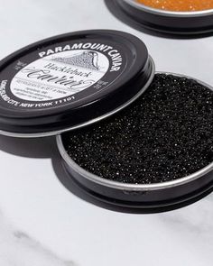 two tins of black glitter sitting on top of a white countertop next to each other