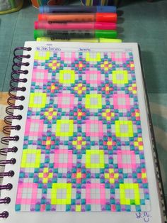 a notebook covered in colored squares and crayons on top of a table next to markers