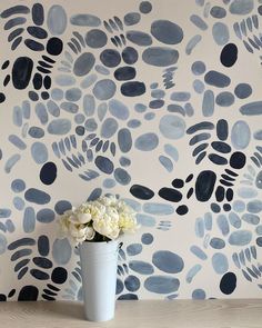 a vase filled with white flowers sitting on top of a wooden table next to a wall