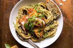 a white bowl filled with pasta and meat on top of a wooden table next to bread