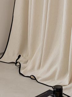 a black and white object is sitting on the floor next to a curtain with an attached cord