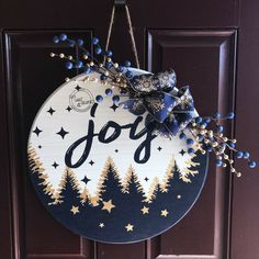 a door hanger with the word joy hanging on it's front door, decorated with gold stars and blue berries