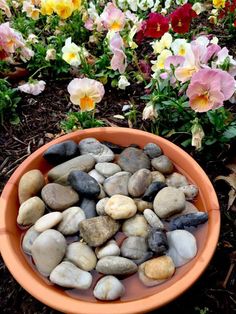 a bowl filled with lots of rocks next to flowers