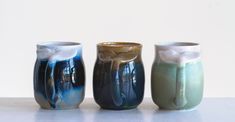 three vases sitting side by side on a white surface, one is blue and the other is green