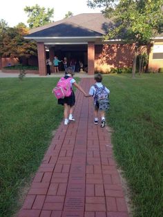 two children walking down a brick path towards a building