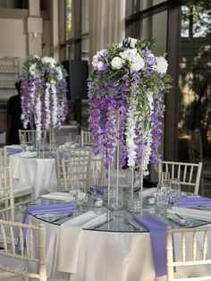 the table is set with purple and white flowers in tall vases on each side