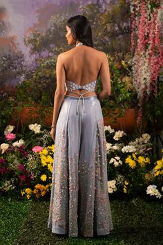 Element of fun and ethereal crafted in one ensemble. Sofia co-ord set consists of a halter neck top paired up with wide-legged pants accentuated with tassel drops. The ice-blue hue of the ensemble makes one look surreal and elegant while at the same time, the silhouette defines your bubbliness. Halter neck blouse embroidered with daisy motifs highlighted with sequins and flowers. Wide-legged pants with attached crisscross studded straps at the waistline crafted out of blingy sequined fabric high Lehenga Pants Designs, Indian Outfits Pants, Summer Embellished Pant Set For Party, Halter Neck Suits Indian, Floor-length Palazzo Set For Summer Parties, Blue Palazzo Set For Spring Party, Party Sets With Back Tassel Tie-up, Floor-length Spring Party Palazzo Set, Floor-length Palazzo Set For Spring Parties