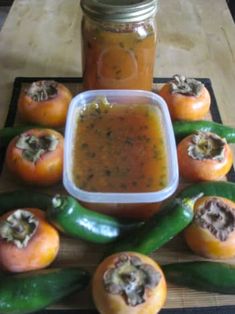 several peppers are arranged on a cutting board with a jar of sauce in the middle