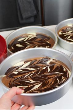 four pans filled with chocolate and white icing on top of a countertop