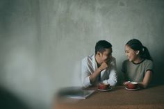 a man and woman sitting at a table with coffee cups in front of their faces