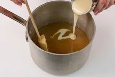 a person pouring liquid into a pot with wooden spoons on the side and another hand holding a ladle