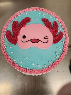 a cake decorated with pink and blue icing on top of a metal surface in the shape of a crab