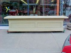 a white trunk sitting on top of a sidewalk next to a red car in front of a store