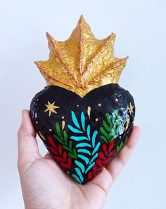 a hand holding a painted heart with a gold leaf on it's top,