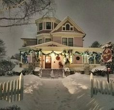 a house is decorated for christmas with lights and wreaths on the front porch, along with snow