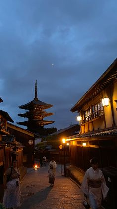 some people are walking down the street at night with lights on and pagodas in the background