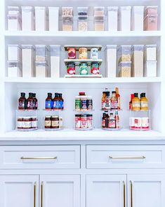 an organized pantry with white cabinets and gold pulls on the bottom shelf is filled with food