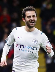 a soccer player is running and smiling at the camera while wearing a white uniform with blue writing on it