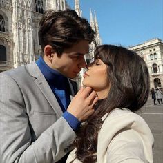 a man and woman standing next to each other in front of a building with tall spires