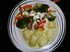 a white plate topped with potatoes and broccoli covered in sauce next to other vegetables