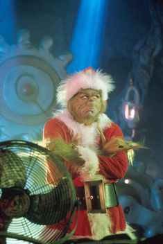 a man dressed as santa clause holding a fan in front of a stage with lights