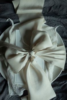 a white plate topped with a bow on top of a black cloth covered tablecloth