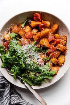 a white bowl filled with pasta and spinach covered in parmesan cheese next to a fork