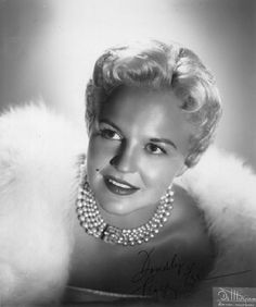 a black and white photo of a woman with pearls on her neck, wearing a fur coat