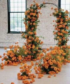 an arrangement of orange flowers and greenery in front of a brick wall with windows