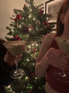 two women holding up martini glasses in front of a christmas tree