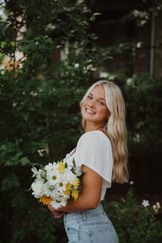 a woman holding a bouquet of white and yellow flowers in front of her face smiling at the camera