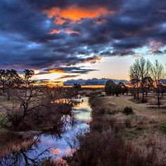 the sun is setting over a small stream in an open field with trees and grass