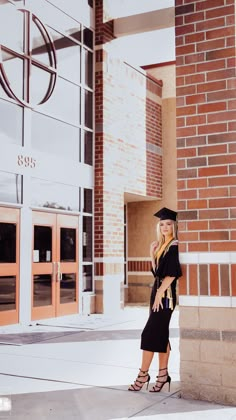 a woman in a graduation cap and gown standing on the side of a building talking on her cell phone