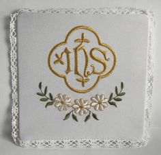 embroidered monogram with flowers and leaves in gold on a white square doily that says,