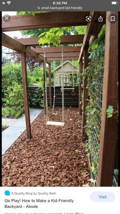 a wooden pergoline and swing set in a backyard area with trees, shrubs and bushes