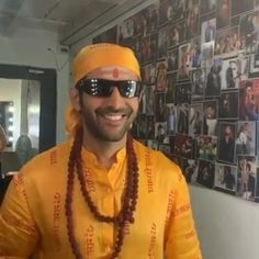 a man wearing sunglasses and a yellow outfit with beads around his neck smiles at the camera