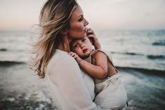 a woman holding a small child on the beach at sunset with waves in the background