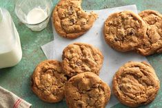 six chocolate chip cookies sitting on top of a piece of paper next to a glass of milk