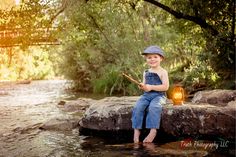 a young boy sitting on top of a rock next to a river holding a fishing rod