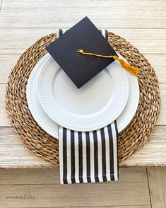 a graduation cap sitting on top of a white plate next to a black and white striped napkin