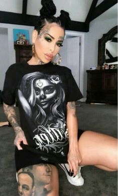 a woman with tattoos sitting on the floor wearing a black t - shirt and white sneakers