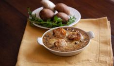 a bowl of food sitting on top of a table next to a plate of potatoes