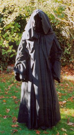 a statue of a person in a black robe standing on the grass with trees and bushes behind it