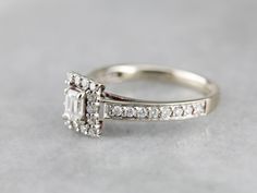 "This is a contemporary, easy to wear engagement ring that has an outstanding amount of impact! The center stone is an emerald cut diamond with plenty of glitter. A rectangular halo of smaller diamonds adds sophistication and even more sparkle. The beautiful side diamonds flow gently in down the shoulders, adding a beautiful tapered feel to the ring! Metal: 14K White Gold Gem: Diamond .26 Carats, SI in Clarity, G in Color Gem Measurements: 3.3 x 4.4 mm, Emerald Cut Accents: 30 Diamonds totaling Emerald Cut Diamond, Dream Engagement, Dream Engagement Rings, Colored Gems, Ring Metal, Emerald Cut Diamonds, Ring Ring, Hand Engraving, Eternity Bands