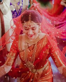 a woman in red and gold dress with veil on her head, smiling at the camera